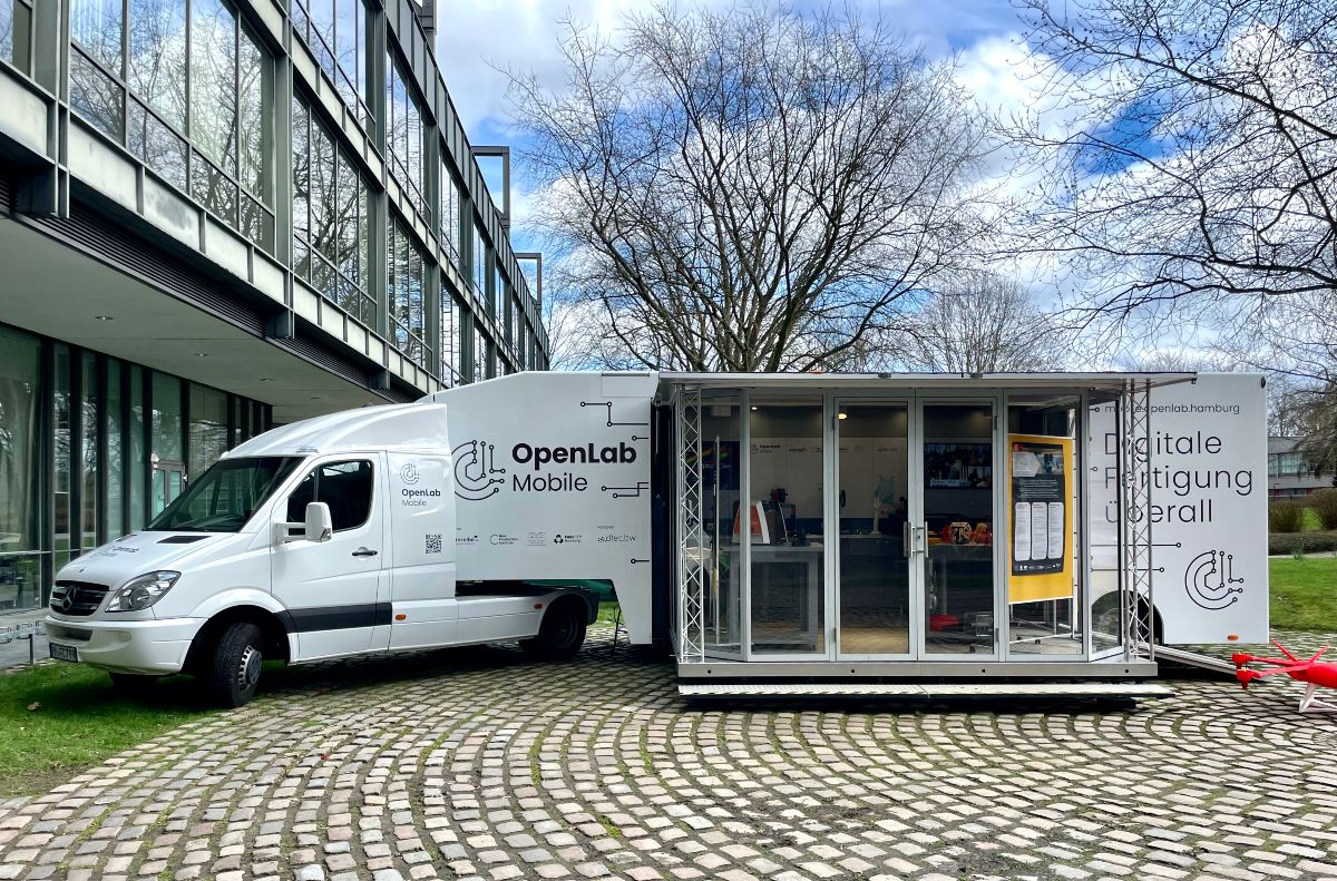 A white truck that is open. In it you can see a few 3D printers. Written is several times OpenLab Mobile next to the OpenLab logo and digitale Fertigung überall. Translation: digital manufacturing everywhere. 