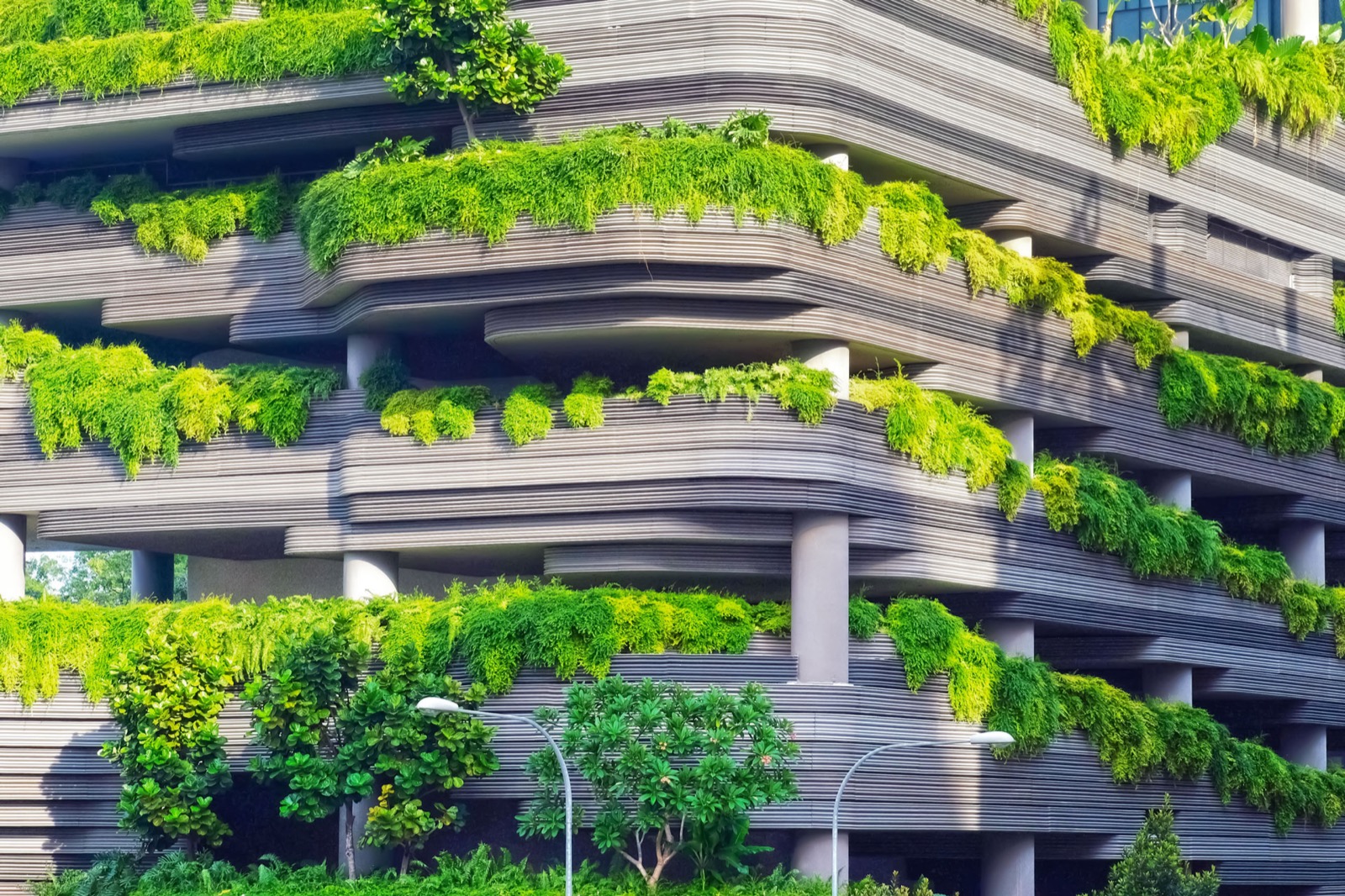 Ein futurischtisches Gebäude aus vielen sichtbaren schichten und Säulen, das stark mit Pflanzen übersäht ist.
